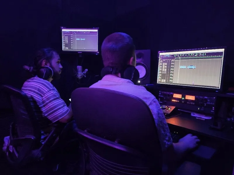 Two at the desk under the purple light, the session up on both screens