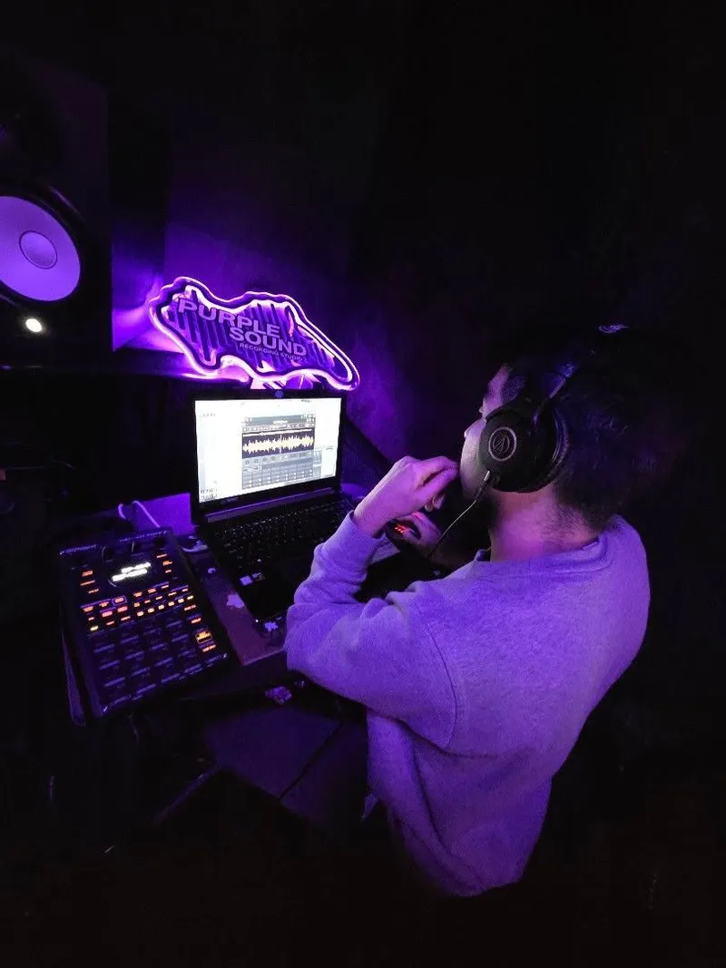 On the pads under the Purple Sound neon sign, headphones on, waveform up on the laptop